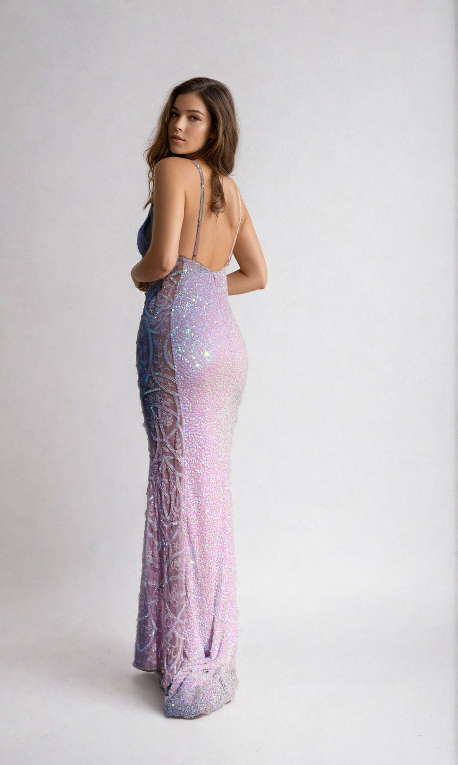 A woman poses in the Aleta Sheer-Side Backless Sequin Prom Dress 1121, featuring shimmering pastel sequins and an open back, as she looks over her shoulder against a plain light background.